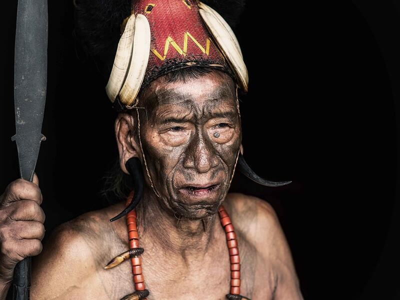 A shirtless tribesman warrior is pictured wearing a traditional headdress and brandishing a spear with a heavily tattooed chest.  (Mediadrumimages/ Trevor Cole)