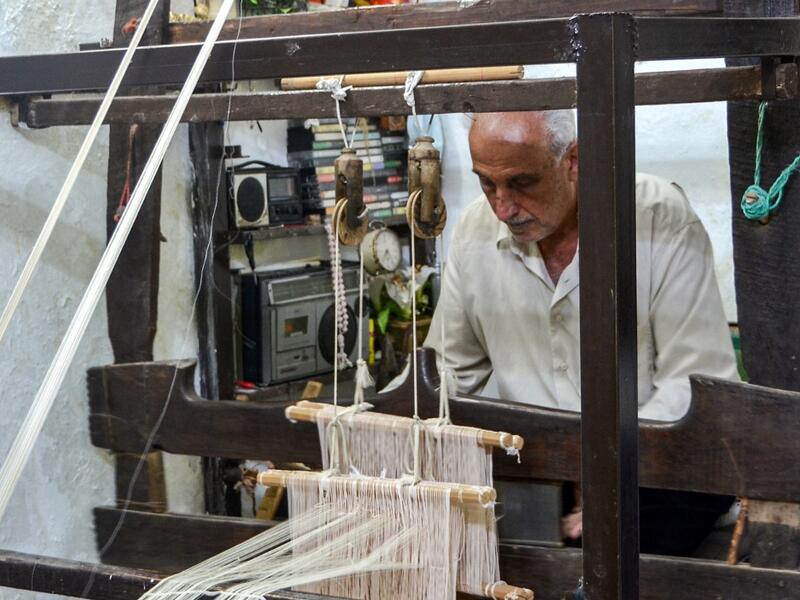 Muhammad Saud, a 65-year-old Syrian silk farmer, handweaves silk threads on a loom at his home workshop in the village of Deir Mama, in west-central Syria on June 22, 2020. MAHER AL MOUNES / AFP