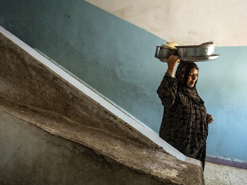 A woman walks down a stairwell while carrying pots on her head at a school building where Syrians -- displaced from the area of Ras al-Ain by the Turkish offensive on the northeast -- are staying in the city of Hasakah, on June 30, 2020. Delil SOULEIMAN / AFP