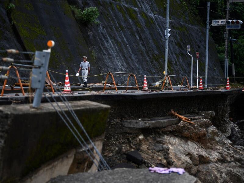 A man walks along a road damaged from recent heavy rains and flooding in the village of Kuma, Kumamoto prefecture on July 9, 2020. Japanese emergency services and troops were scrambling on July 9 to reach thousands of homes cut off by catastrophic flooding and landslides that have killed dozens and caused widespread damage. CHARLY TRIBALLEAU / AFP