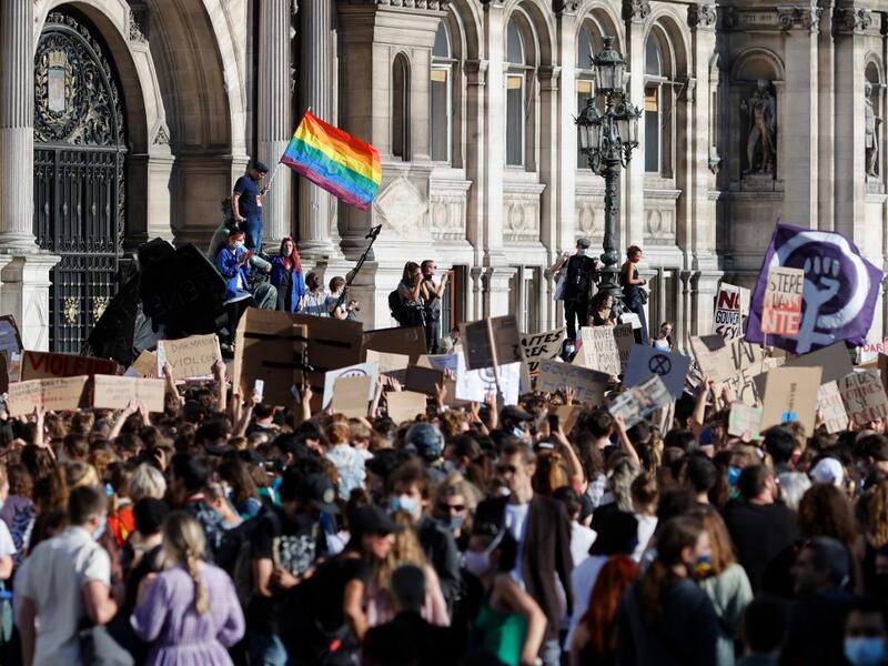 A protester (L) waves a rainbow flag, symbol of LGBTQ social movements, and others hold placards during a demonstration called by feminist movements in front of the city hall in Paris, on July 10, 2020, to denounce the nomination of French Interior Minister, facing rape accusations and French Justice Minister who criticised the #MeToo movement against sexual harassment. Thomas COEX / AFP