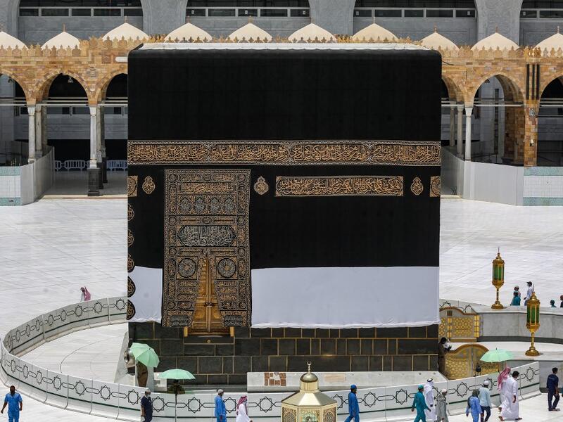 Workers at the Grand Mosque complex in Saudi Arabia's holy city of Mecca, mask-clad due to the COVID-19 coronavirus pandemic, wave and speak to a security guard as they walk around the Kaaba, Islam's holiest shrine, at centre of the complex ahead of the annual Hajj pilgrimage season on July 24, 2020. AFP