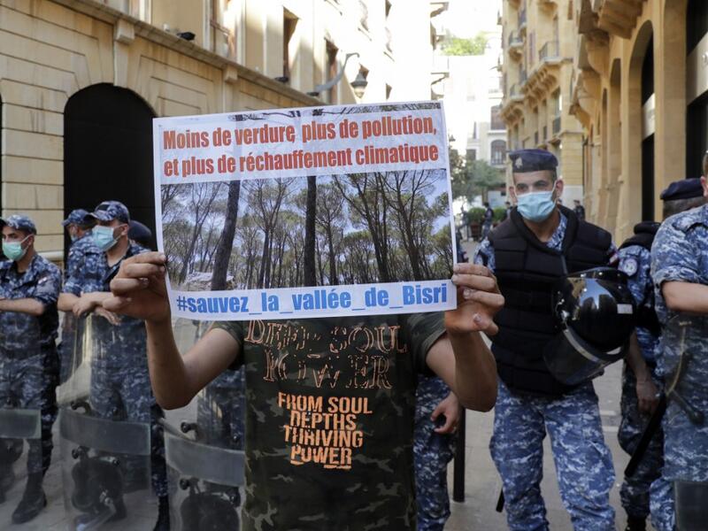 A demonstrator standing in front of members of the Lebanese security forces holds a placard as he takes part in a rally in front of the World Bank offices in the downtown district of the Lebanese capital Beirut on July 25, 2020, to protest against the Bisri dam project, partly financed by the World Bank. The government says the Bisri dam is vital to tackling chronic water shortages. But activists say it will ravage most of the region's farmland and historic sites, and they also fear the consequences of buil