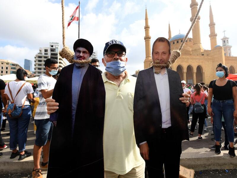 A man poses for a picture with a cardboard cut-out of Hassan Nasrallah (L), the head of Lebanon's Shiite Muslim movement Hezbollah, and former Foreign Minister Gibran Bassil hung by Lebanese protesters in downtown Beirut on August 8, 2020, during a demonstration against a political leadership they blame for a monster explosion that killed more than 150 people and disfigured the capital Beirut. AFP