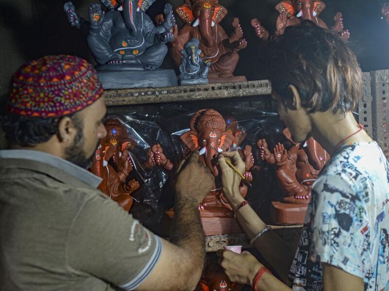 In this picture taken on August 11, 2020, Muslim potter Yusuf Zakaria Galwani (L) instructs an artisan as he gives finishing touches to a clay idol of elephant headed Hindu god Ganesha at his workshop at Kumbharwada inside the Dharavi slums in Mumbai. After the coronavirus pandemic clobbered his pottery business, a Muslim artisan from India's largest slum turned to a Hindu god to revive his fortunes by making environmentally-friendly Ganesha idols for an upcoming festival. In Mumbai's Dharavi slum, Galwani 
