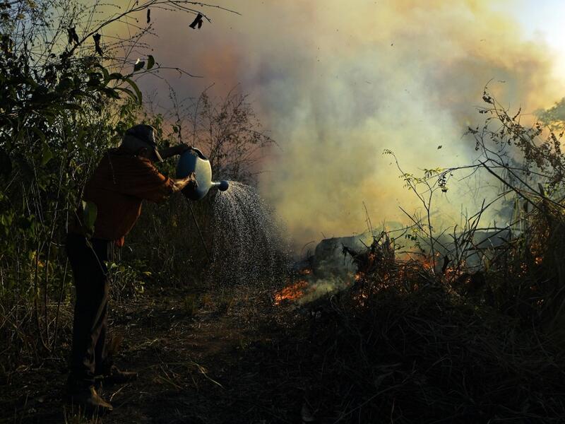 A farmer tries to pour water on an area close to an illegally lit fire in Amazon rainforest reserve, south of Novo Progresso in Para state, Brazil, on August 15, 2020. CARL DE SOUZA / AFP
