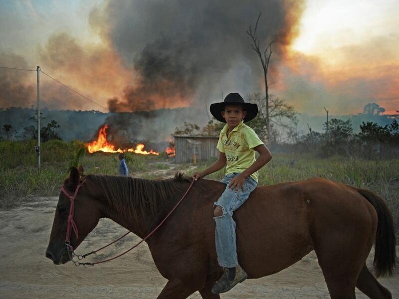 A young boy rides his horse past an illegally lit fire in a section of Amazon rainforest, south of Novo Progresso in Para state, Brazil, on August 15, 2020. CARL DE SOUZA / AFP