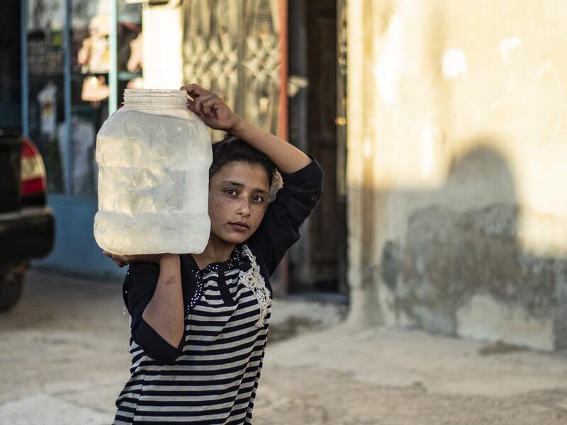 A Syrian girl carries a pot of water filled up from cisterns provided by humanitarian organisations during a water outage in Syria's northeastern city of Hasakah on August 22, 2020. As coronavirus spreads across northeast Syria, residents in Hasakeh have been caught up in the latest spat between Turkish forces to the north and Syrian Kurds it views as "terrorists". In October last year, Turkish forces occupied a 120-stretch (70-mile) stretch of land inside the Syrian border, including the Alouk power statio