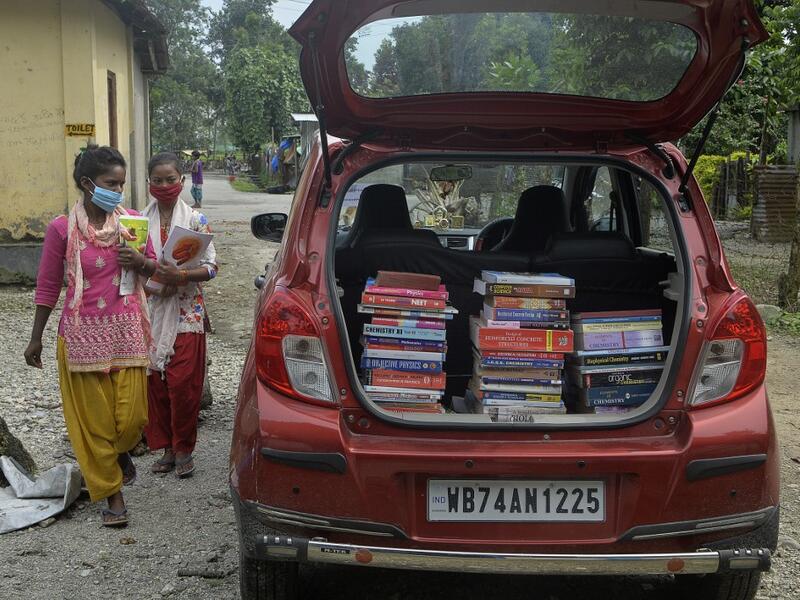 Youths from Merry view Tea Garden organisation walk near a book library car to attend a class as part of 'Tuition for Rs 10' project, origanized by Indian couple Anirban Nandy and Poulami Chaki Nandy for underprivileged students unable to assist online classes at Hatighisa village, some 26 km from Siliguri, on September 1, 2020, as schools remain closed due the Covid-19 coronavirus pandemic. DIPTENDU DUTTA / AFP