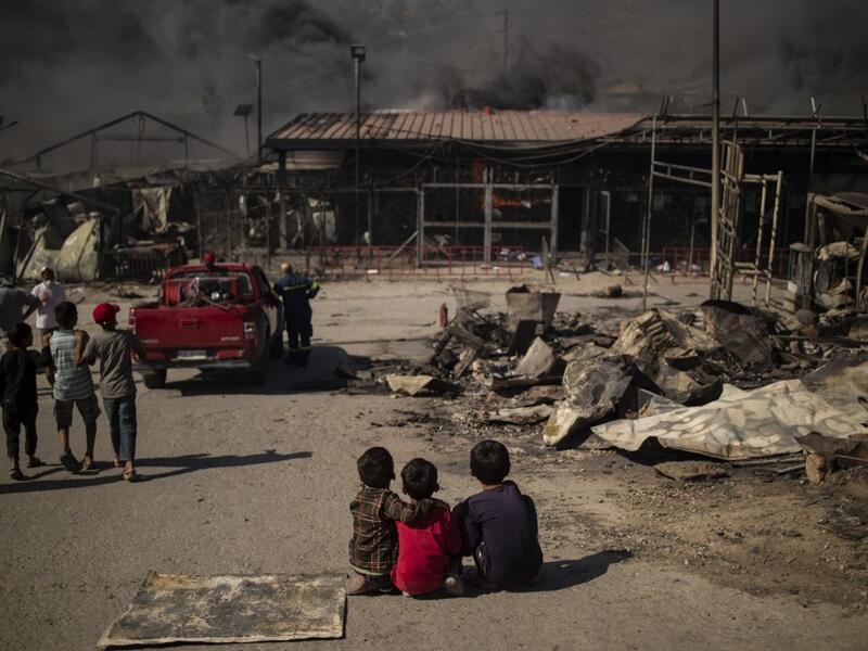 Children sit on the ground in the burnt camp of Moria on the island of Lesbos after a major fire broke out, on September 9, 2020. Thousands of asylum seekers on the Greek island of Lesbos fled for their lives on September 9, 2020 as a huge fire ripped through the camp of Moria, the country's largest and most notorious migrant facility. 