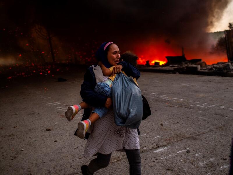 A migrant holds a girl as they flee a fire burning in the Moria camp on the island of Lesbos on September 9, 2020. Thousands of asylum seekers on the Greek island of Lesbos fled for their lives on September 9, 2020 as a huge fire ripped through the camp of Moria, the country's largest and most notorious migrant facility. 