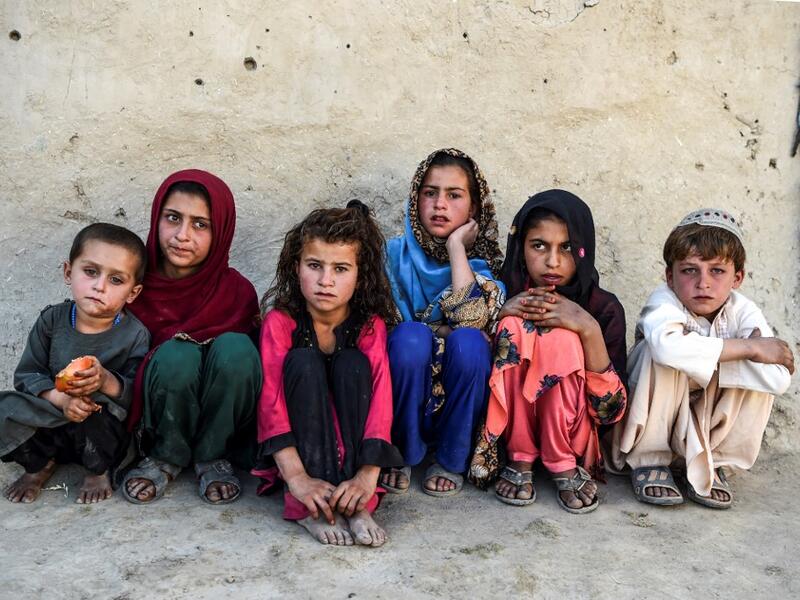 In this photo taken on September 27, 2020, children sit in front of a house at Deh Qubad village in Maiwand district of Kandahar province. The dry and dusty village of Aziz Abad in Maiwand district sits on the frontline of Afghanistan's war and is currently under government control -- but only just. WAKIL KOHSAR / AFP