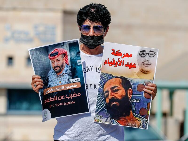 An Israeli left-wing activist lifts posters during a demonstration calling for the release of Palestinian administrative detainees, including Maher al-Akhras, (image L) who's health has deteriorated while on hunger strike, during a protest outside the Israeli run Ayalon prison in Ramle near the coastal city of Tel Aviv, on October 24, 2020. AHMAD GHARABLI / AFP