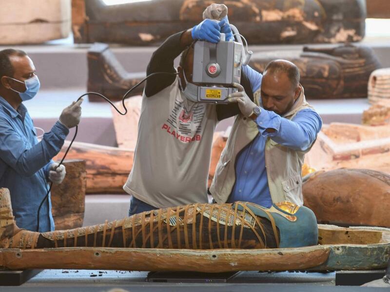 Archaeologists x-ray a mummy, wrapped in a burial shroud adorned with brightly coloured hieroglyphic pictorials, during the unveiling of an ancient treasure trove of more than a 100 intact sarcophagi, at the Saqqara necropolis 30 kms south of the Egyptian capital Cairo, on November 14, 2020. Egypt announced the discovery of an ancient treasure trove of more than a 100 intact sarcophagi, the largest such find this year. The sealed wooden coffins, unveiled on site amid fanfare, belonged to top officials of th