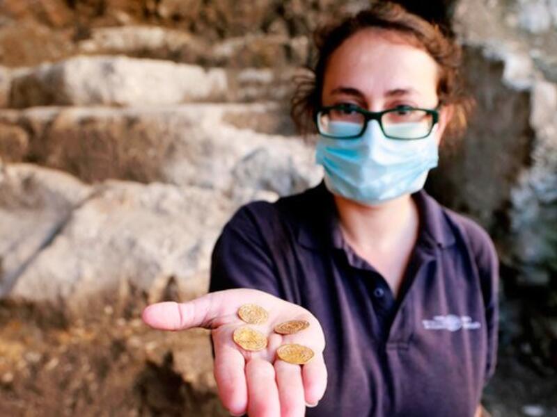 Archaeologist at the Israel Antiquities Authority Evgeniya Rabinovich shows a small pottery jug with four pure gold coins found inside it, at the archaeological rescue excavation site in the Old City of Jerusalem, on November 9, 2020. (AFP)
