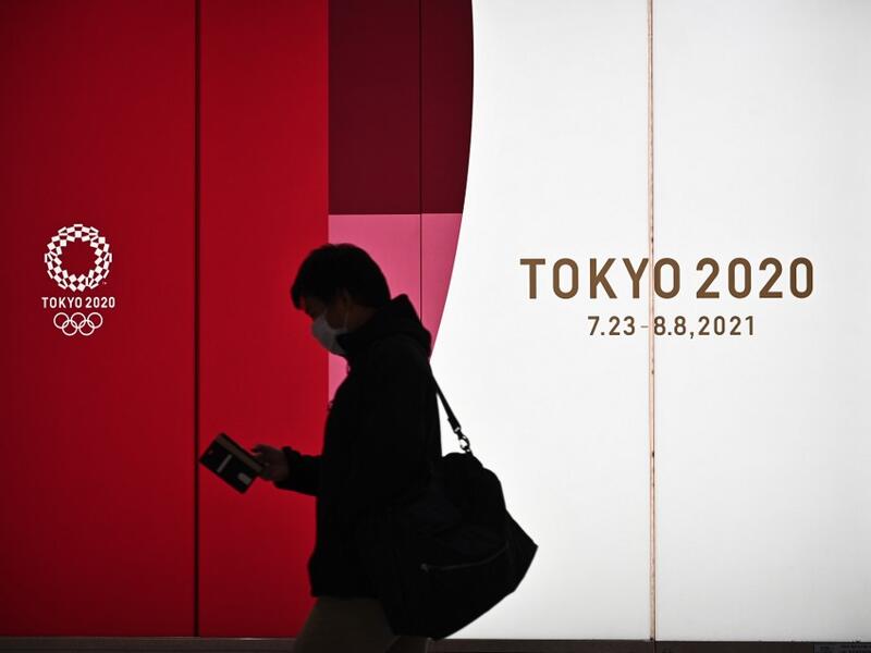 A man walks along a corridor past an official Tokyo 2020 Summer Olympics advertisement board in the Shinjuku district of Tokyo on November 30, 2020. Philip FONG / AFP