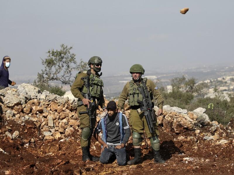 Israeli soldiers detain a Palestinian protester as an Israeli settler hurls rocks at Palestinians during a demonstration against the expansion of settlements in the occupied-West Bank town of Salfit, near the Israeli settlement of Ariel, on November 30, 2020. JAAFAR ASHTIYEH / AFP