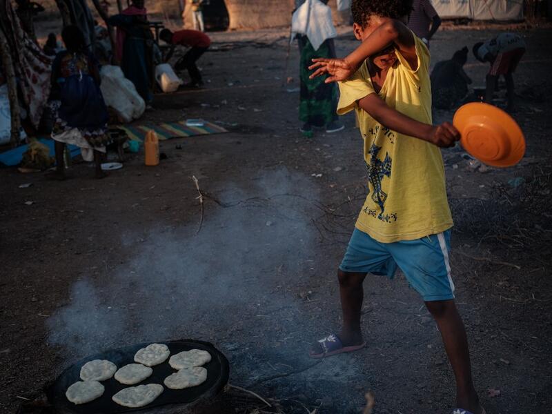 An Ethiopian boy, who fled the Ethiopia's Tigray conflict as a refugee, avoids smoke as he helps to cook at Um Raquba refugee camp in Gedaref, eastern Sudan, on December 1, 2020. Yasuyoshi CHIBA / AFP