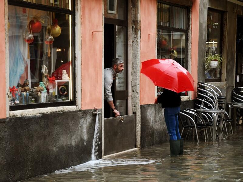 A shop owner protects water from getting in on December 8, 2020 in Venice following a high tide "Alta Acqua" event following heavy rains and strong winds, and the mobile gates of the MOSE Experimental Electromechanical Module that protects the city of Venice from floods, were not lifted ANDREA PATTARO / AFP