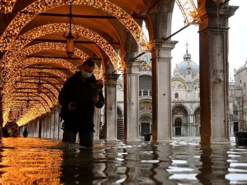 A man walks across an arcade by a flooded St. Mark's Square on December 8, 2020 in Venice following a high tide "Alta Acqua" event following heavy rains and strong winds, and the mobile gates of the MOSE Experimental Electromechanical Module that protects the city of Venice from floods, were not lifted ANDREA PATTARO / AFP