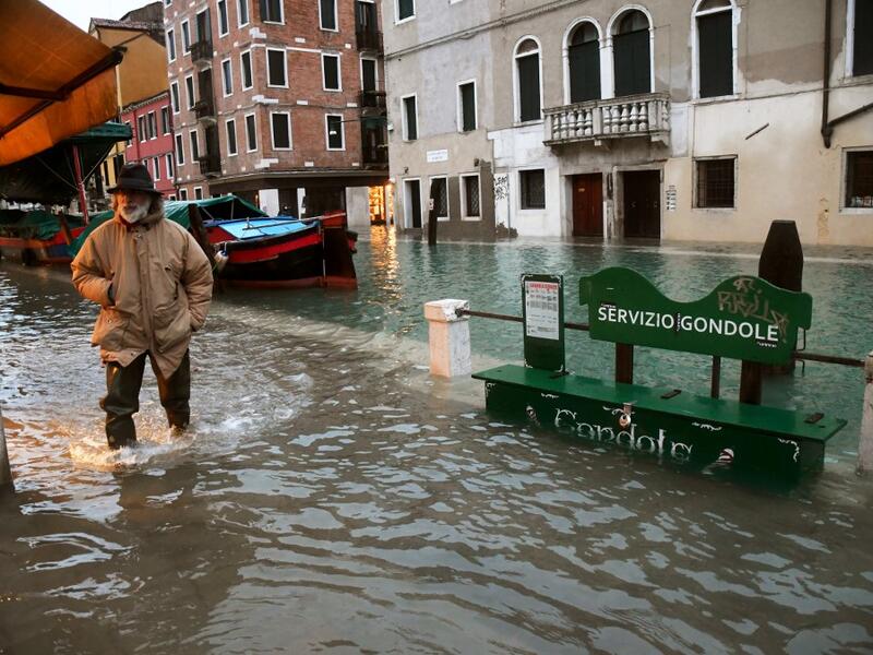A man walks across a flooded canal on December 8, 2020 in Venice following a high tide "Alta Acqua" event following heavy rains and strong winds, and the mobile gates of the MOSE Experimental Electromechanical Module that protects the city of Venice from floods, were not lifted ANDREA PATTARO / AFP
