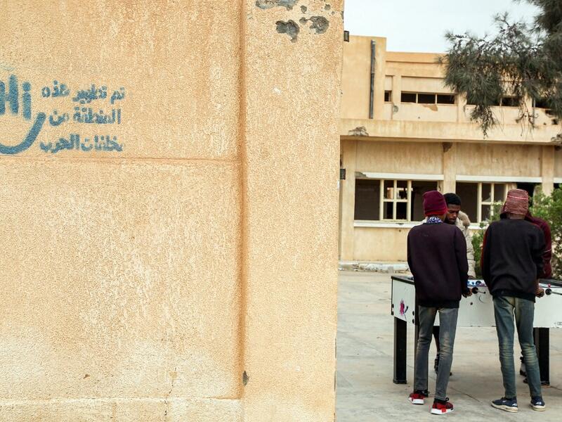 Youths play table football (foosball) outside by abandoned buildings, with graffiti nearby reading in Arabic "this zone has been cleared of the remains of war", in the city of Tawergha, some 200 kilometres (125 miles) east of Libya's capital close to the port city of Misrata, on December 12, 2020. When Libyan dictator Moamer Kadhafi was toppled, people took revenge on those they saw as his supporters -- including the entire town of Tawergha, whose 40,000 residents were forced to flee. Now, almost a decade l