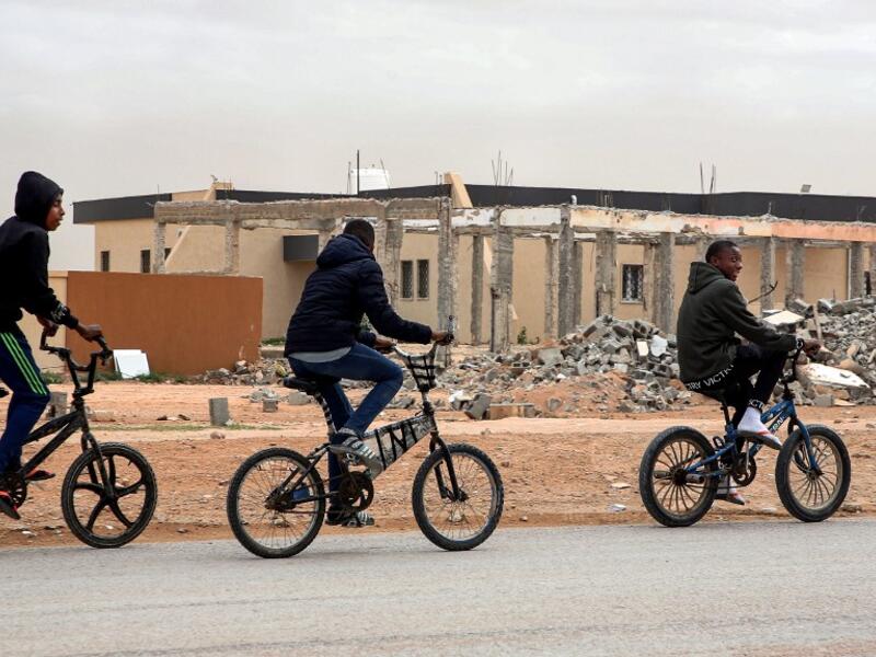 Youths play table football (foosball) outside by abandoned buildings, with graffiti nearby reading in Arabic "this zone has been cleared of the remains of war", in the city of Tawergha, some 200 kilometres (125 miles) east of Libya's capital close to the port city of Misrata, on December 12, 2020. When Libyan dictator Moamer Kadhafi was toppled, people took revenge on those they saw as his supporters -- including the entire town of Tawergha, whose 40,000 residents were forced to flee. Now, almost a decade l