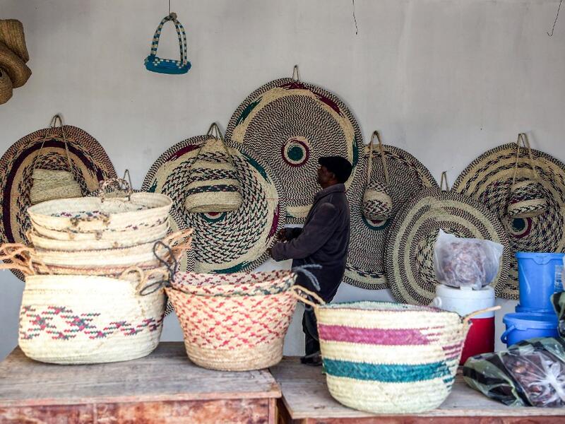 A man inspects palm wicker products on display, made by Haleema Mohamed, one of the residents who returned to the city of Tawergha after fleeing in the aftermath of the toppling of Kadhafi, sits making palm wicker products at a home in Tawergha, some 200 kilometres (125 miles) east of Libya's capital close to the port city of Misrata, on December 12, 2020. When Libyan dictator Moamer Kadhafi was toppled, people took revenge on those they saw as his supporters -- including the entire town of Tawergha, whose 