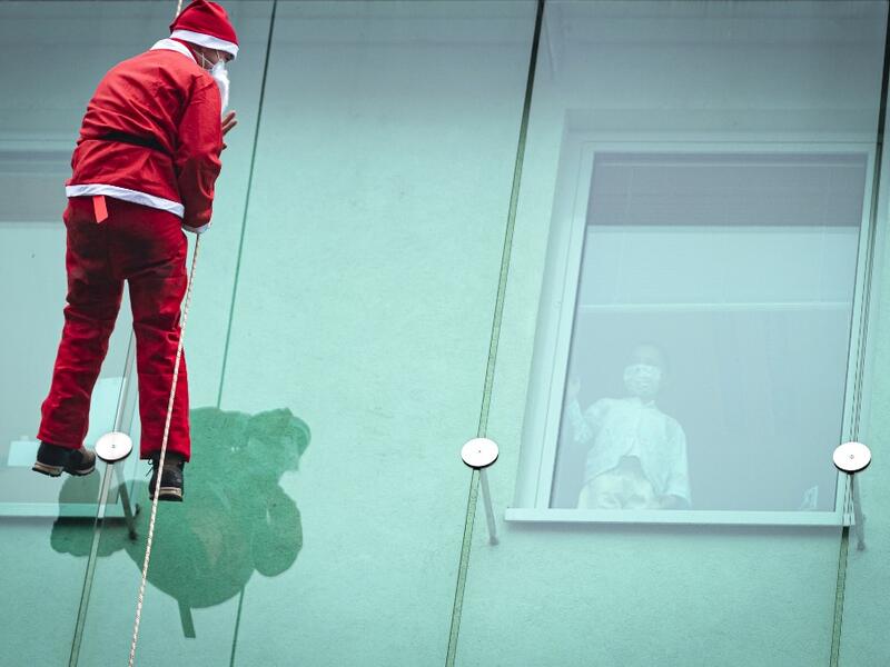 A man dressed as a Santa Claus waves to a child as he descends from the roof of the paediatric clinic in Ljubljana, Slovenia on December 21, 2020. Jure Makovec / AFP