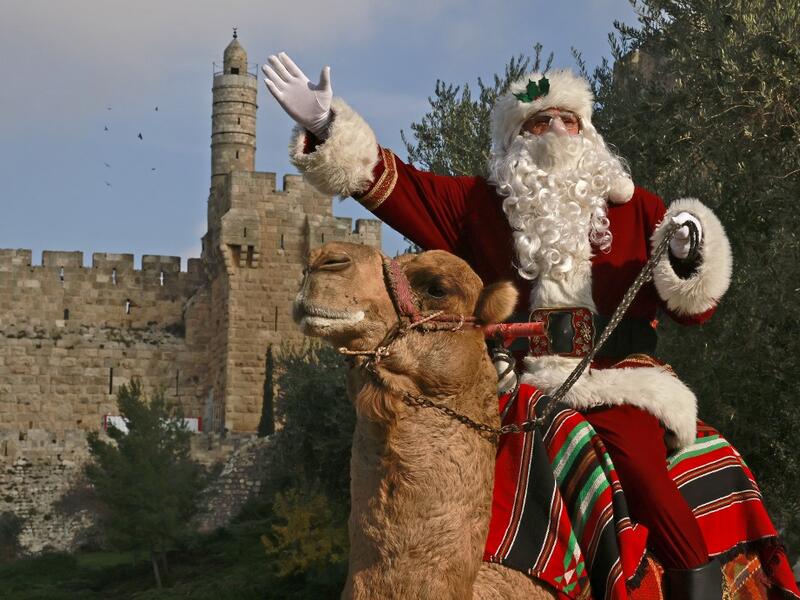 Issa Kassissieh, better known as the Santa Claus of Jerusalem, rides a camel on December 22, 2020 outside Jerusalem's Old City walls. MENAHEM KAHANA / AFP