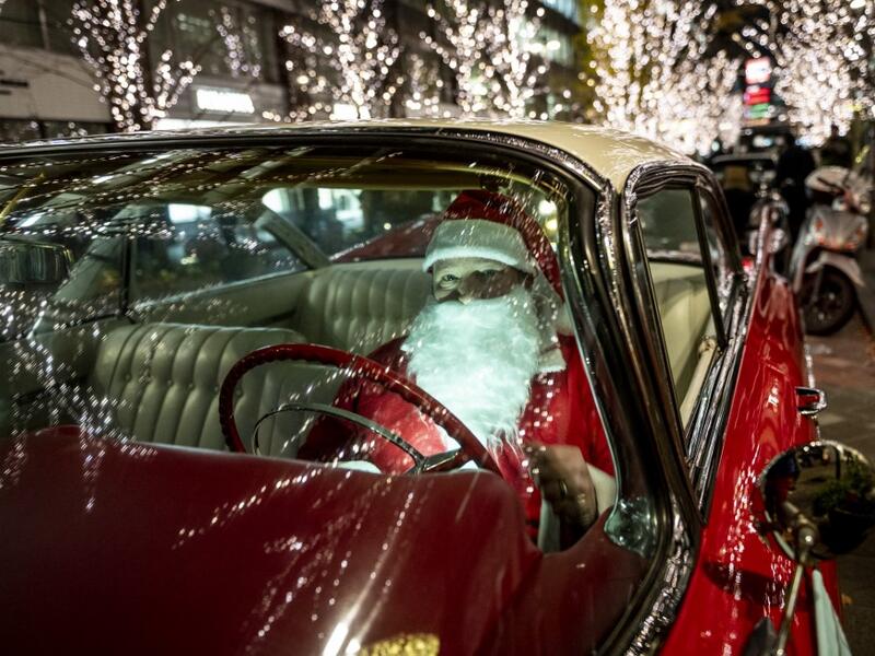 Rob Holtzapfel, a member of a vintage car group dressed as Santa Claus, sits in a 1959 Cadillac along a street lined with Christmas-themed light decorations in Marunouchi district in Tokyo on December 25, 2020. Philip FONG / AFP