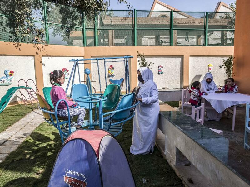 This picture taken during a government-guided tour on December 27, 2020 shows an inmate, mask-clad due to the COVID-19 coronavirus pandemic, pushing a child on a swing at the recreational area of al-Qanatir women's prison, at the tip of the Nile delta in Qalyoubiya province, about 30 kilometres north of Egypt's capital. Khaled DESOUKI / AFP