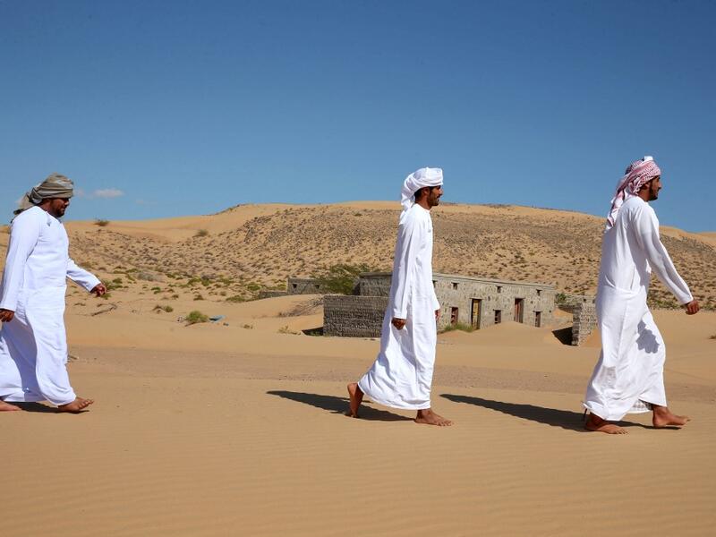 Former inhabitants of Wadi al-Murr, walk near abandoned houses in the Omani village, about 400 kms (250 miles) southwest of the capital Muscat, on December 31, 2020. Encroaching desert sands have left little evidence that Wadi al-Murr ever existed, but former inhabitants, while resigned to its destruction, are trying to preserve its memory. MOHAMMED MAHJOUB / AFP