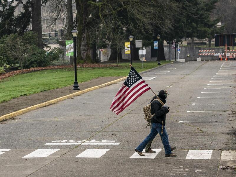 A man walks with a U.S. flag on the Washington State Capitol campus on January 20, 2021 in Olympia, United States. One Donald Trump protester held a sign at an otherwise quiet capitol campus on Presidential Inauguration Day today. David Ryder/Getty Images/AFP