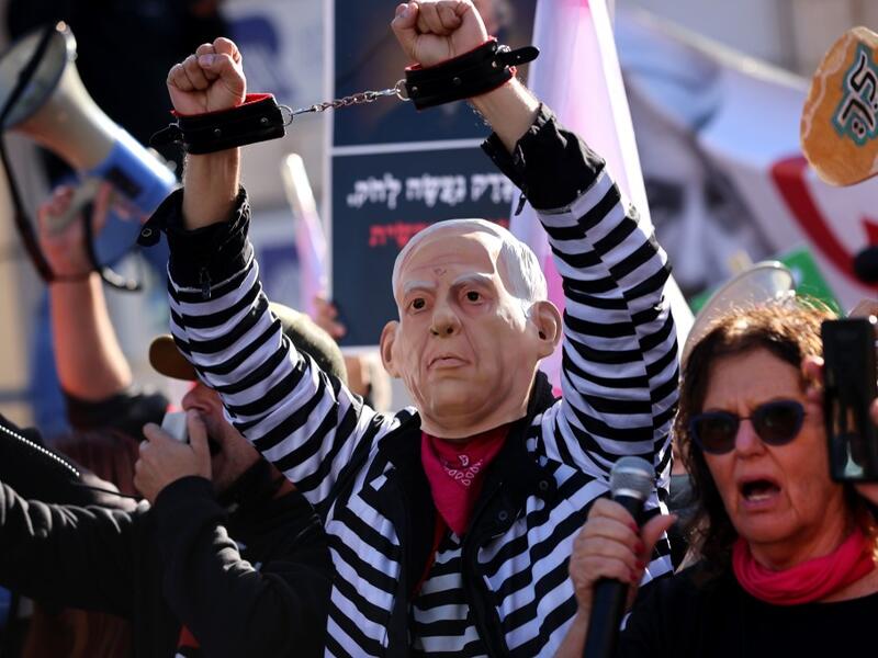 A demonstrator wearing a mask representing Prime Minister Benjamin Netanyahu gestures during a demonstration outside the court, as his corruption trial resumes in occupied east Jerusalem, on February 8, 2021. Israel's Prime Minister Benjamin Netanyahu returns to court to formally respond to the corruption charges against him, as his trial enters an intensified phase six weeks before he faces re-election. EMMANUEL DUNAND / AFP