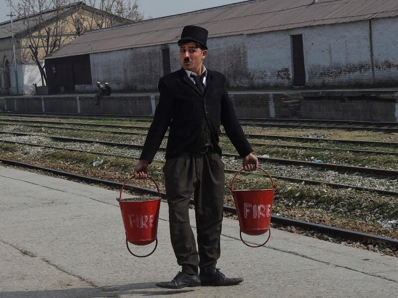 In this picture taken on February 9, 2021, street actor Usman Khan, dressed up as silent film star Charlie Chaplin, performs at a train station in the Pakistan's northwestern city of Peshawar. Wearing a bowler hat and familiar toothbrush moustache, Pakistan's Usman Khan darts through traffic swinging a cane, teasing motorists and shopkeepers for laughs and a few rupees with a Charlie Chaplin impersonation that has become a viral sensation.  Abdul MAJEED / AFP