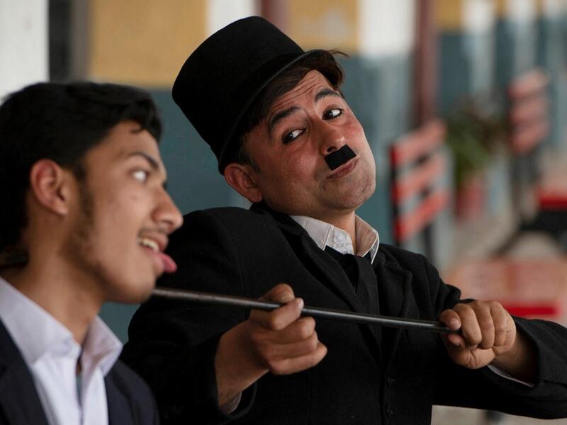 In this picture taken on February 9, 2021, street actor Usman Khan (R), dressed up as silent film star Charlie Chaplin, performs in the Pakistan's northwestern city of Peshawar. Wearing a bowler hat and familiar toothbrush moustache, Pakistan's Usman Khan darts through traffic swinging a cane, teasing motorists and shopkeepers for laughs and a few rupees with a Charlie Chaplin impersonation that has become a viral sensation.  Abdul MAJEED / AFP