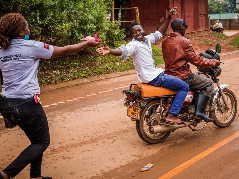 A man sitting on a motorbike catches condoms from a health worker delivering free condoms on the international condom day, in the streets of Kampala on February 13, 2021, ahead of Valentine’s day. Badru KATUMBA / AFP