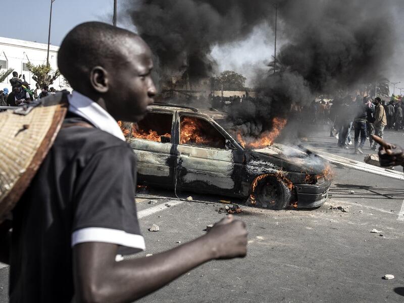 A protester runs past a burning car during a protest in Dakar on March 8, 2021, after the country's opposition leader Ousmane Sonko was charged with rape. Usually considered a beacon of stability in a volatile region, deadly clashes between opposition supporters and security forces have rocked the West African state. JOHN WESSELS / AFP