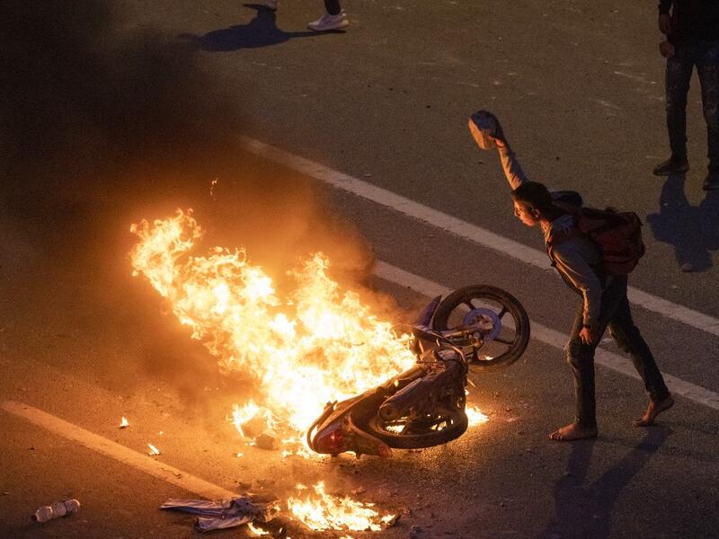 A migrant throws a rock onto a burning motorbike as they clash with Moroccan riot police in protest at being stopped from crossing the border, in the northern town of Fnideq, close to the border between Morocco and Spain's North African enclave of Ceuta on May 19, 2021. Migrants were still trying to cross from Morocco into the Spanish enclave of Ceuta on May 19, 2021, after a record 8,000 people poured over the border this week, escalating tensions between Rabat and Madrid