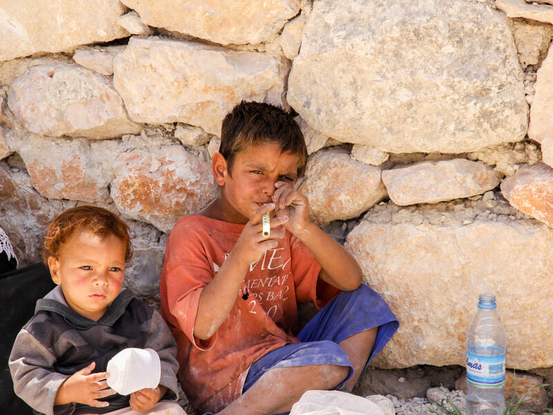 Yong boy playing bamboo flute with his younger brother at the roadside of Roman ruins in Jerash, Jordan