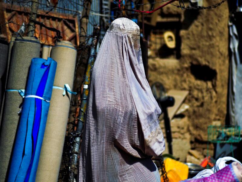CORRECTION / A burqa-clad woman walks past a stall selling secondhand items at a market in Kandahar on September 22, 2021. 