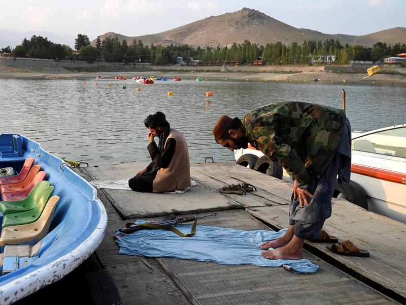 Taliban fighters offer prayers on a dock for boats at Qargha Lake on the outskirts of Kabul. "This is Afghanistan!" a Taliban fighter shouts on the pirate ship ride at a fairground in western Kabul, as his armed comrades cackle and whoop on board the rickety attraction. (Photo by WAKIL KOHSAR / AFP) / TO GO WITH: AFGHANISTAN-CONFLICT-FAIRGROUND, SCENE BY JAMES EDGAR - TO GO WITH: Afghanistan-conflict-fairground, SCENE by James EDGAR