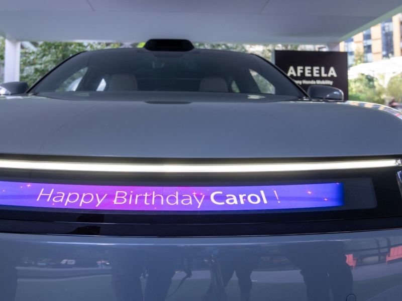 The four-door electric car appears more ready for production now sleeker and more advanced starting with a reimagined front that highlights its modern technological character. The front bumper features a sporty black strip at the bottom, along with an illuminated logo and a full-width light strip that merges with the uniquely shaped headlights.