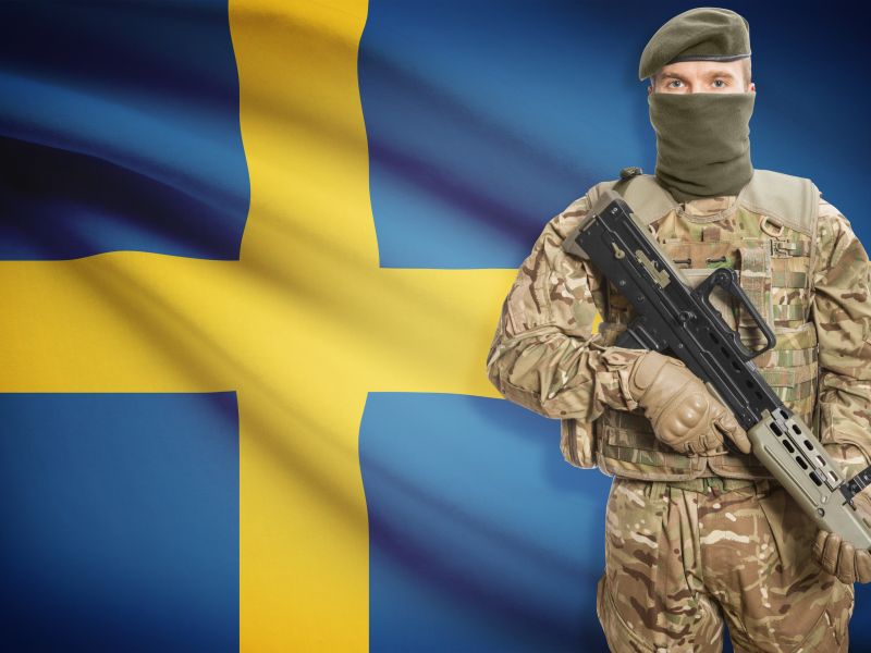جندي يحمل بندقية رشاشة وخلفه العلم الوطني - السويد