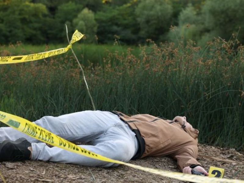 شخص ممدد على الأرض داخل موقع تحقيق جنائي محاط بشريط أمني في منطقة خارجية