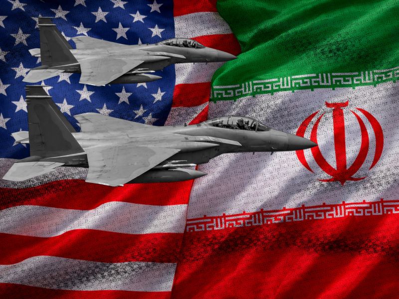 مقاتلتان حربيتان تحلقان أمام علمي الولايات المتحدة وإيران في صورة تعبر عن التوتر العسكري والتصعيد بين البلدين.