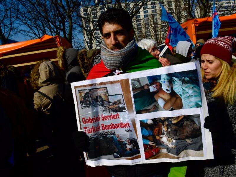 A protester holds a poster depicting injured people and showing a photograph (top L) of German Foreign Minister Sigmar Gabriel serving his Turkish counterpart Mevlut Cavusoglu during the demonstration; text reads "Gabriel serves, Turkey bombs". (JOHN MACDOUGALL / AFP)