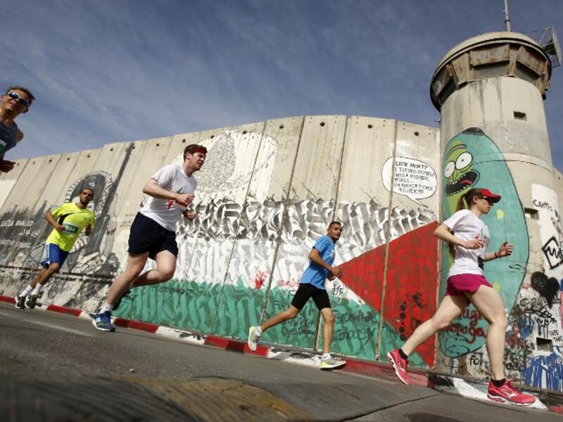 Participants run along Israel's controversial separation barrier, which divides the West Bank from Jerusalem, in the biblical town of Bethlehem during the 6th International Palestine Marathon on Mar. 23, 2018. 
(Musa AL SHAER / AFP)