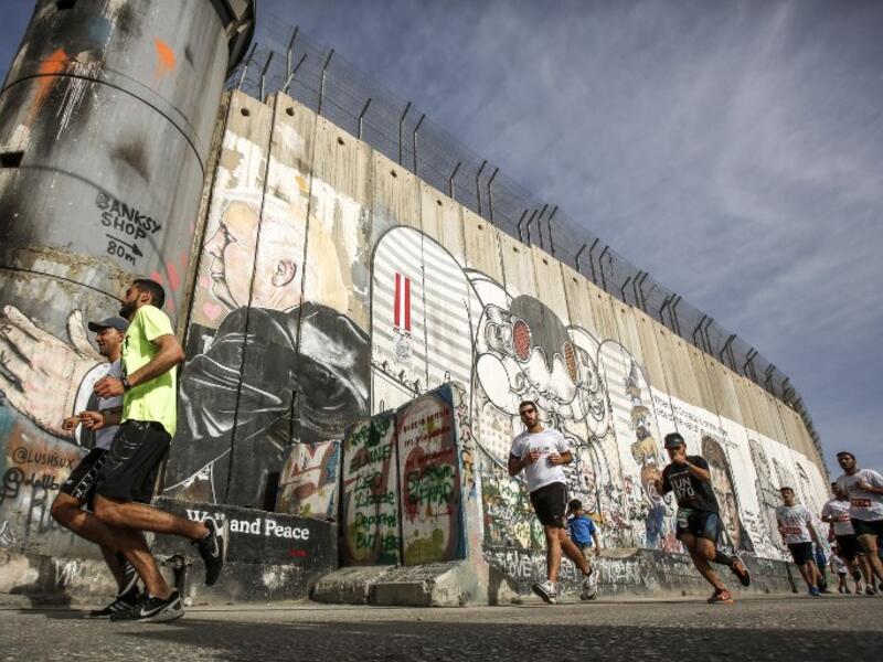Participants run along Israel's controversial separation barrier, which divides the West Bank from Jerusalem, in the biblical town of Bethlehem during the 6th International Palestine Marathon on Mar. 23, 2018. 
(Musa AL SHAER / AFP)